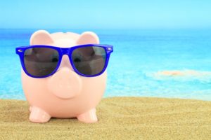 Summer piggy bank with sunglasses on the beach